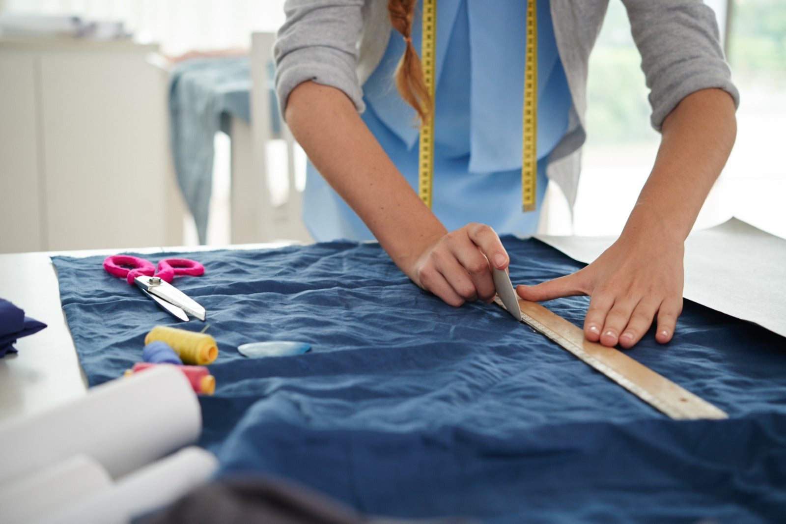 Person measuring blue fabric with a ruler on a table.